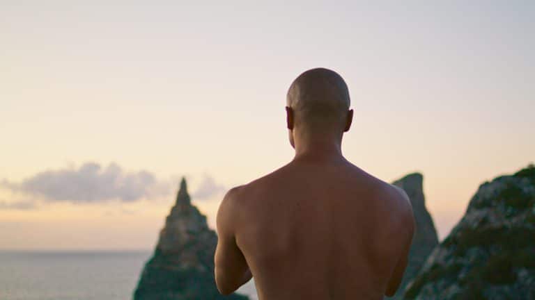 Strong man practicing yoga meditating at sunset ocean cliff. Calm zen like guy