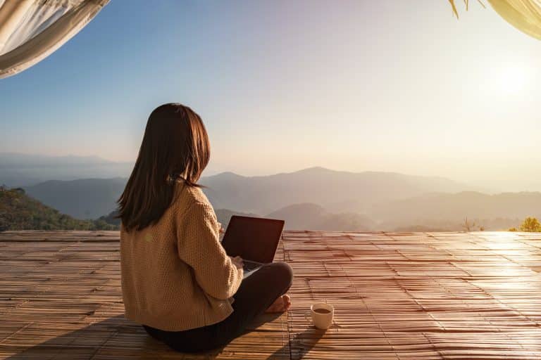 Young woman freelancer working online using laptop and enjoying the beautiful nature landscape